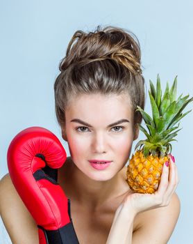 Young Woman with pineapple and boxing glove, fighting for healthy eating concept