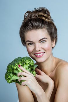 Portrait of a beautiful woman with perfect skin holding broccoli and smiling