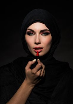 Young beautiful muslim woman putting red lipstick