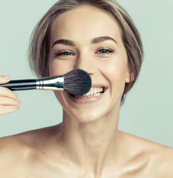 Portrait of a beautiful smiling woman applying make-up with a brush and making a funny face