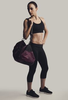 Portrait of sporty young woman posing with a gym bag,  against a gray background