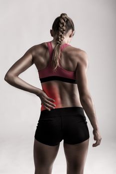 Studio shot of a sporty young woman holding her lower back in pain