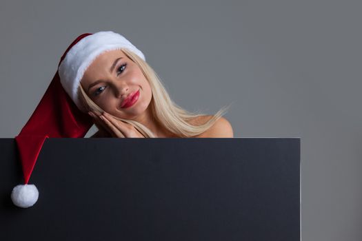 Santa girl holding blank black sign billboard. Christmas woman in Santa hat showing paper sign.