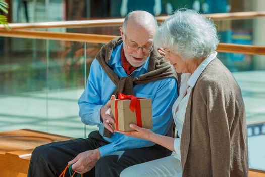 Senior couple in shopping mall with gifts