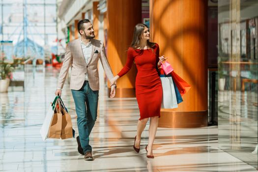 Happy beautiful young couple with shopping bags in mall