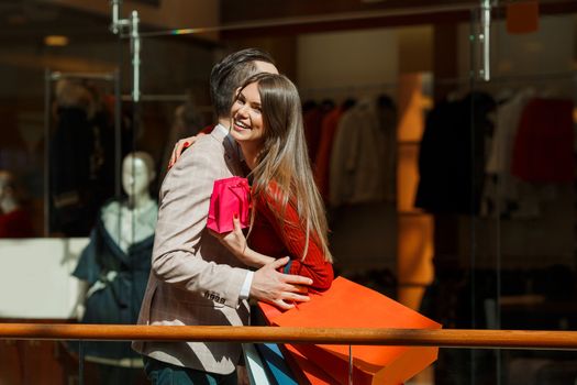 Happy beautiful young couple with gift bag hug in shopping mall