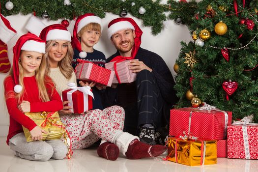 Cheerful family with Christmas gifts sitting near decorated Christmas tree