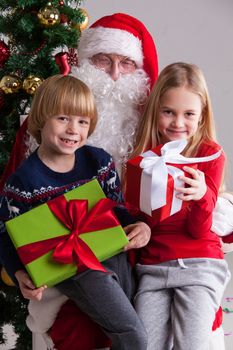 Portrait of smiling little children sitting on santa claus knees near christmas tree