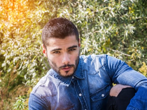 Handsome young man at countryside, in front of field or grassland, wearing shirt, looking at camera