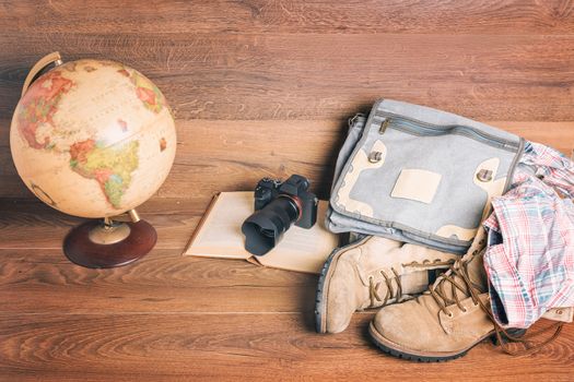 Front view of globe,camera,book,bag,boots and shirt, wooden background,vintage look for travel concept.