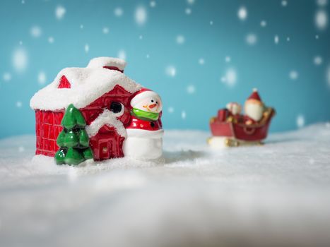 Happy Santa Claus with gifts box on the snow sled going to snow house. near snow house have Snowman and Christmas Tree. Santa Claus and snow house on the snow the background is powder blue.