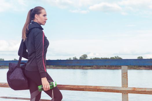 A woman in sportswear with bottle of water on embankment background