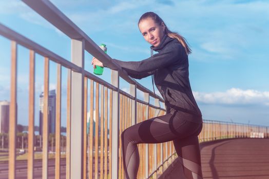 A woman in sportswear with bottle of water have rest at sunset on the evening city background