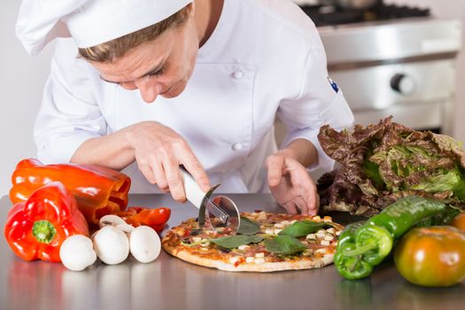Cook cutting a Mediterranean pizza with vegetables and cheese