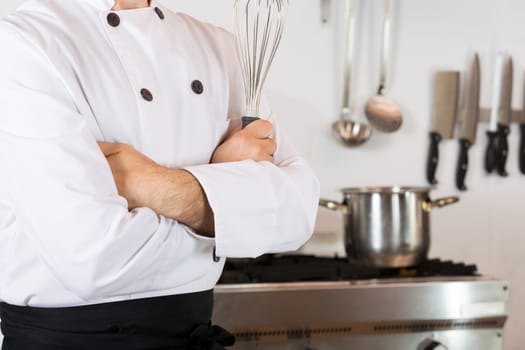 Chef in the kitchen with his arms crossed and with a whisk