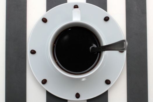 Coffee cup with spoon on saucer and coffee beans against white background forming clock dial. View from above. Coffee as symbol of morning energy and cheerfulness or evening refreshment.