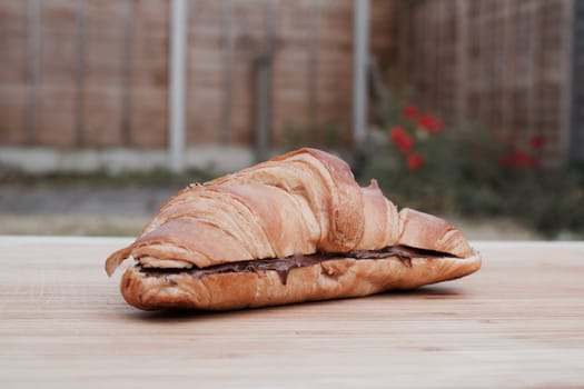 Delicious and fresh croissant on the wooden table in garden. Sunny day.