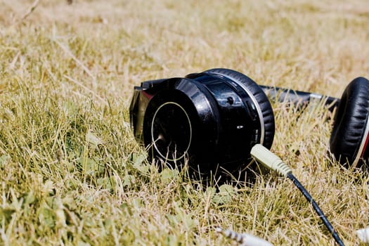 Black old and dirty headphones in green grass on the garden at summer time.