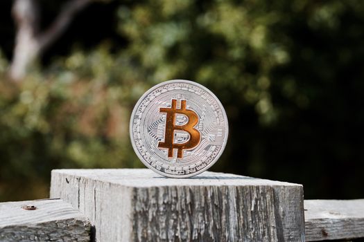 Digital currency physical silver bitcoin coin on the wooden fence in garden.