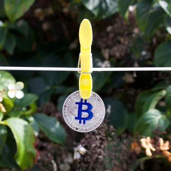 Digital currency physical silver bitcoin coin with blue sign in garden on laundry line.