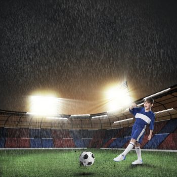 Excited boy football player at stadium kicking ball