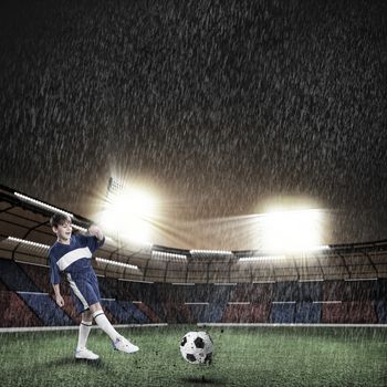 Excited boy football player at stadium kicking ball