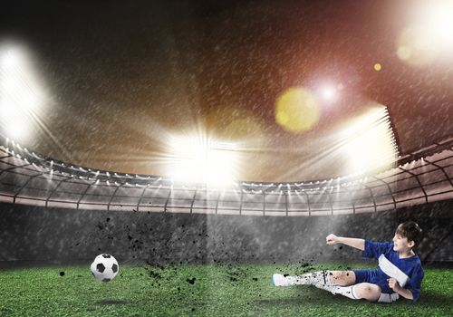 Excited boy football player at stadium kicking ball