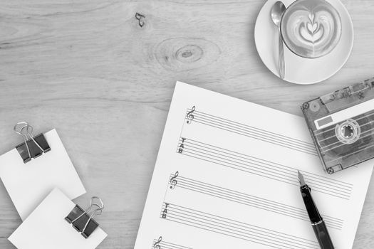Sheet music, fountain pen, tape cassette and coffee latte on wooden table, top view picture
