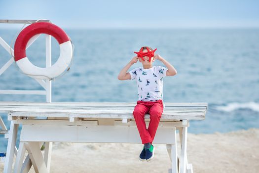 Handsome boy teen happyly spending time together with his friend bulldog on sea side Kid dog holding playing two sea stars close to life buoy float wearing red pants trousers slippers and t-shirt.