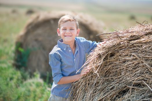 Attractive boy sitting on a haystack and smiling.