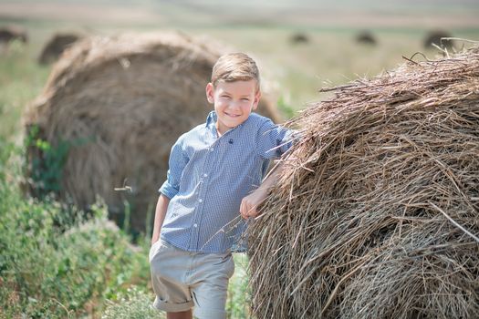 Attractive boy sitting on a haystack and smiling.