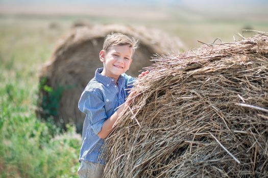 Attractive boy sitting on a haystack and smiling.