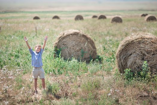 Attractive boy sitting on a haystack and smiling.