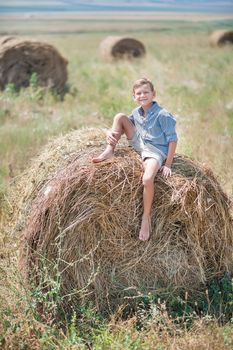 Attractive boy sitting on a haystack and smiling.