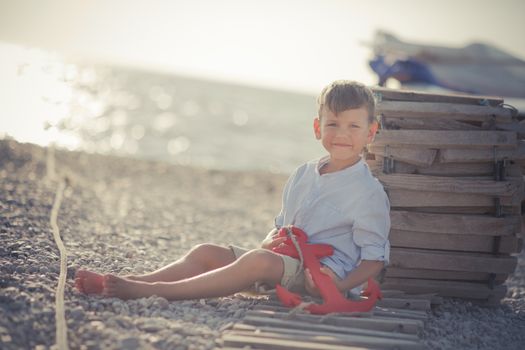 Nice looking handsome boy on beach close to wooden boat wearing fancy stylish blue shirt and shorts with gallows enjoy summer time alone on awesome ocean.