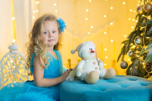 Young beautiful girl in blue white elegant evening dress sitting on floor near christmas tree and presents on a new year eve Interior with christmas decorations. Shallow DOF and bokeh background