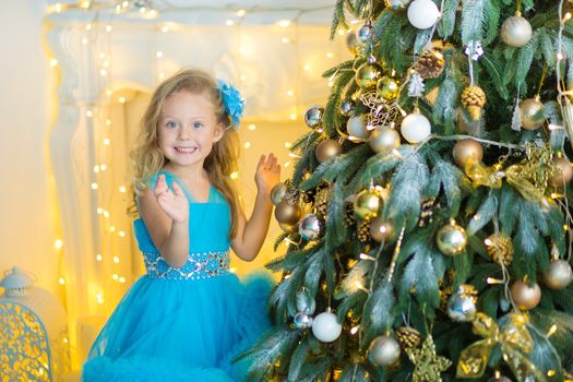 Young beautiful girl in blue white elegant evening dress sitting on floor near christmas tree and presents on a new year eve Interior with christmas decorations. Shallow DOF and bokeh background