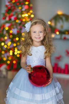 Young beautiful girl in blue white elegant evening dress sitting on floor near christmas tree and presents on a new year eve Interior with christmas decorations. Shallow DOF and bokeh background