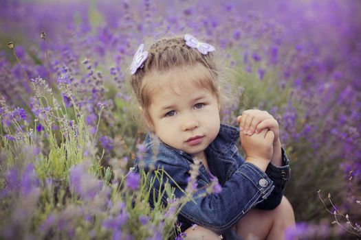 Pretty young girl sitting in lavender field in nice hat boater with purple flower on it