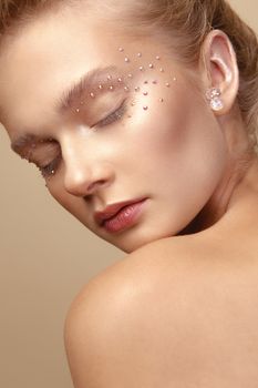 Studio Portrait of a young cute blonde model girl in art makeup with rhinestones