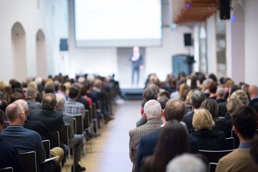 Speaker giving a talk in conference hall at business event. Audience at the conference hall. Business and Entrepreneurship concept. Focus on unrecognizable businessman in the audience.