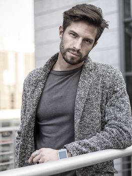 One handsome young man in urban setting in European city, standing, smiling and looking at camera