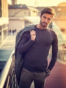 One handsome young man in urban setting in European city, standing, smiling and looking at camera