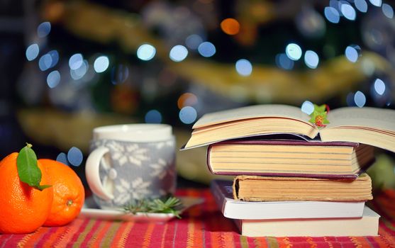 Open book, cup of hot drink and orange fruits with holidays background