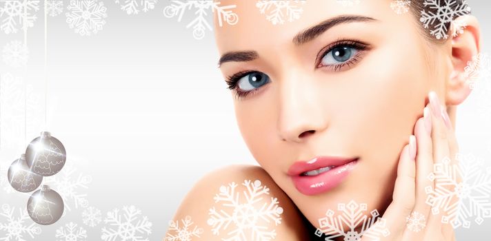 Closeup headshot portrait of a beautiful woman with beauty face and clean smooth soft skin, mild makeup. Grey steel background with snowflakes, christmas baubles and a place for your information