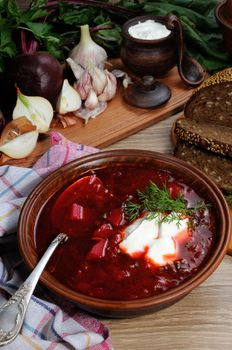 Borscht-vegetable beetroot soup, on the table with slices of rye cereal bread and gluten of sour cream, garlic and herbs. Rustic style.