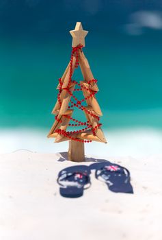 Christmas at the beach, sun, surf and leisure.  A pair of thongs and small driftwood Christmas tree  with beautiful sunny ocean background.