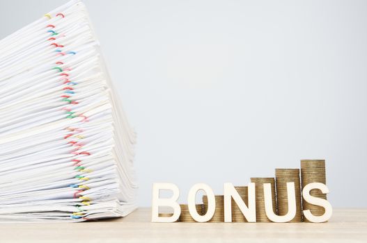 Bonus letters and step pile of gold coins with overload document report of sale and papercilp on wooden table with white background and copy space. Business and finance concept rich and successful.