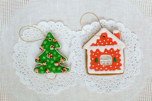 Two gingerbread cookies in the shape of the Christmas tree and small house on a white napkin background. Top view, flat lay, copy space