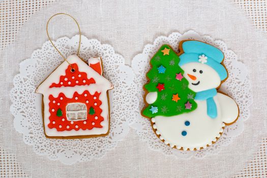 Two gingerbread cookies in the shape of the Christmas tree, snowman and small house on a white napkin background. Top view, flat lay, copy space